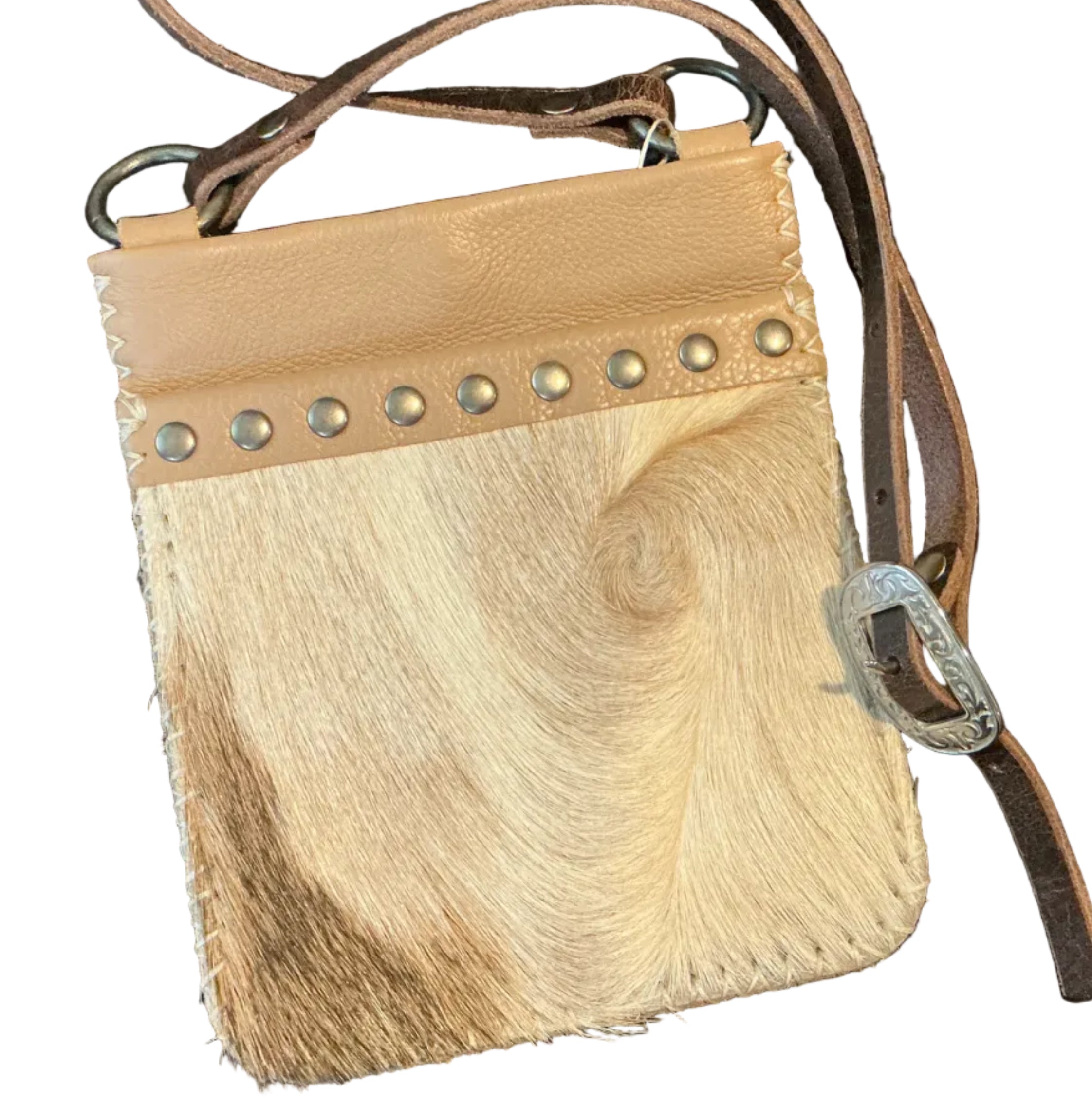A small handbag with a natural cowhide body, tan leather trim, silver-tone studs, and a brown leather strap, laid flat on a dark quilted blanket.