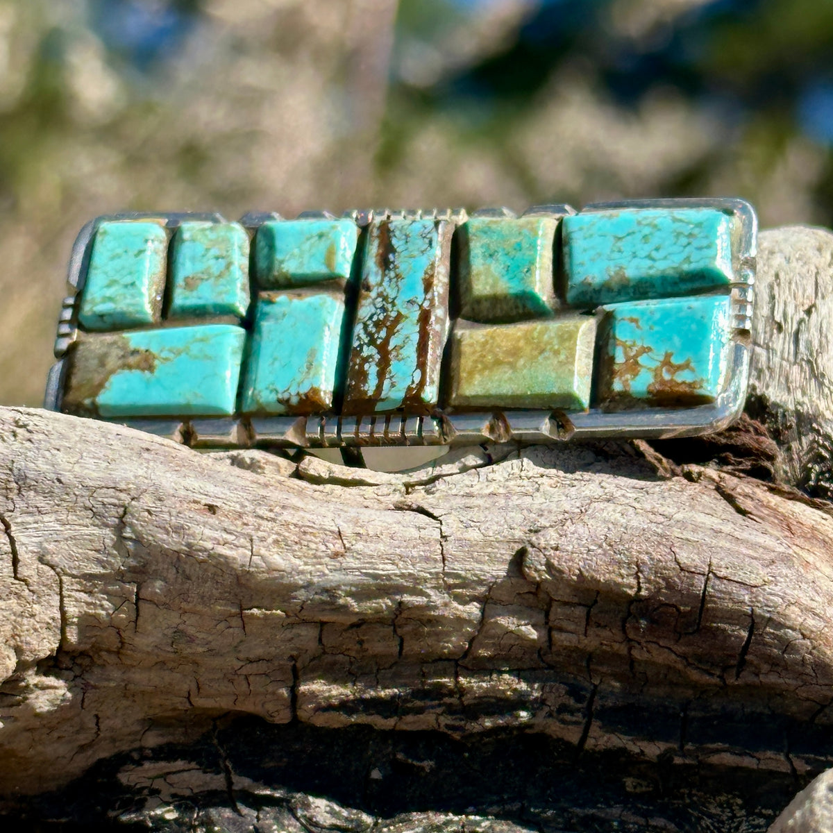 Brandon Etsitty Navajo sterling silver ring with cobblestone-set turquoise in blue, aqua and green, resting on driftwood outdoors