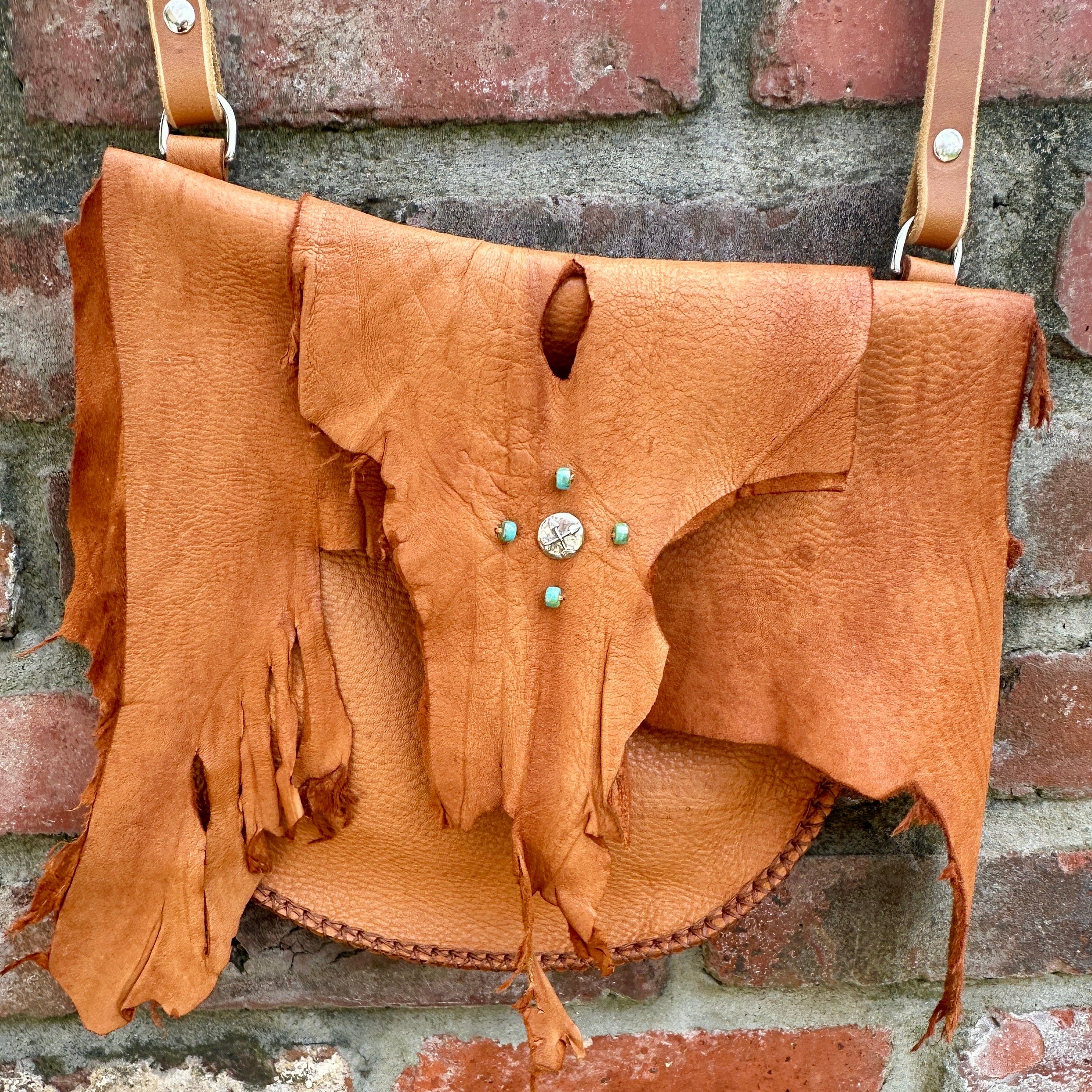 Elk Leather Crossbody, by Bridger Leather is a sienna colored elk skin bag with frayed edge flap and is accented with a sterling silver button adorned with 2 crossed arrows,  there are also 4 turquoise beads sewn on.