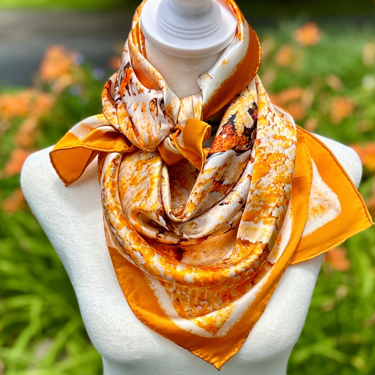 Mammoth Hot Springs silk scarf knotted at the neck on a mannequin, showing the orange, rust and cream print and gold border