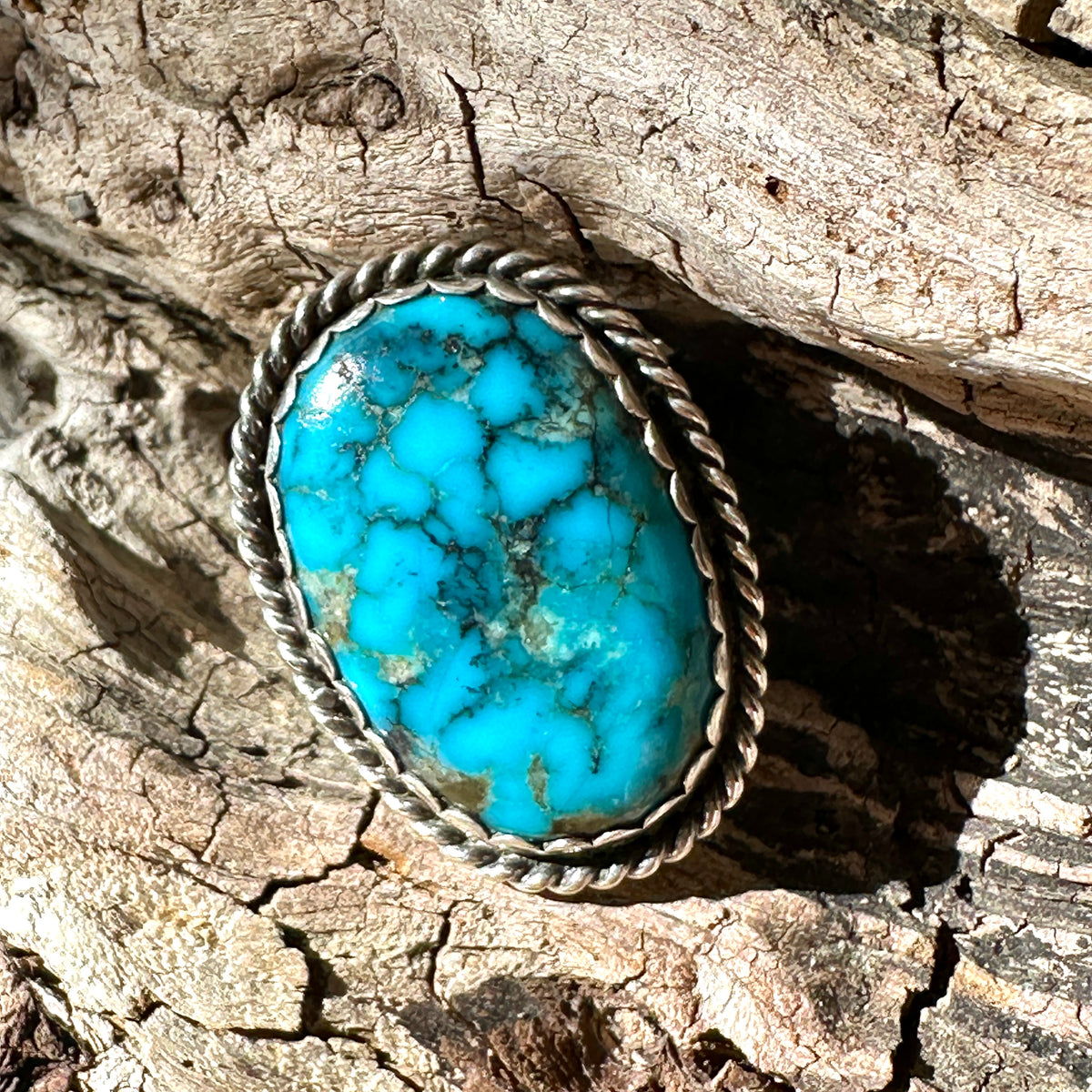 Sterling silver ring with an oval blue turquoise stone and golden-brown matrix, framed by a twisted-rope border, resting on weathered wood