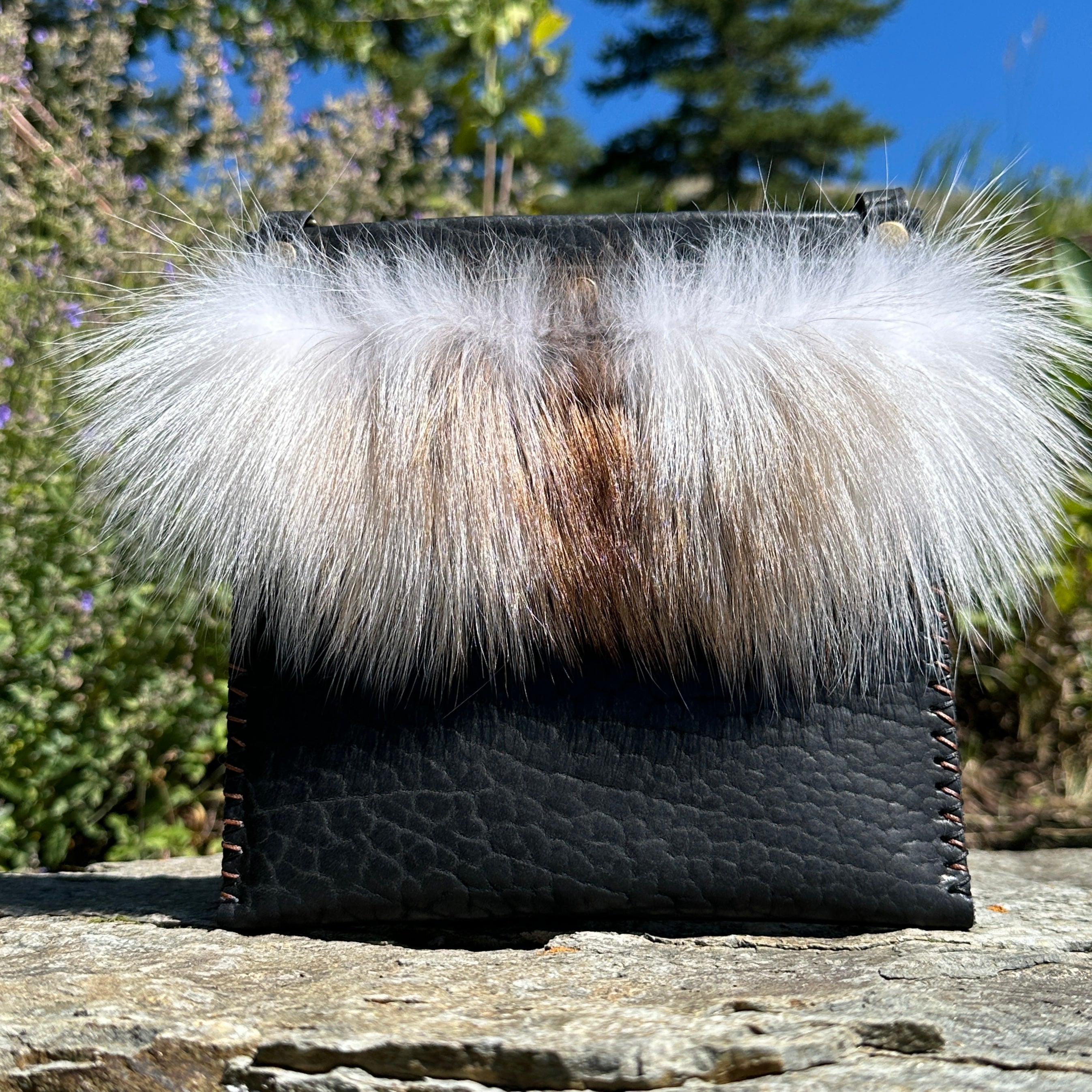 The Ana Evening Bag in black bison leather with natural fox fur trim, viewed straight on outdoors