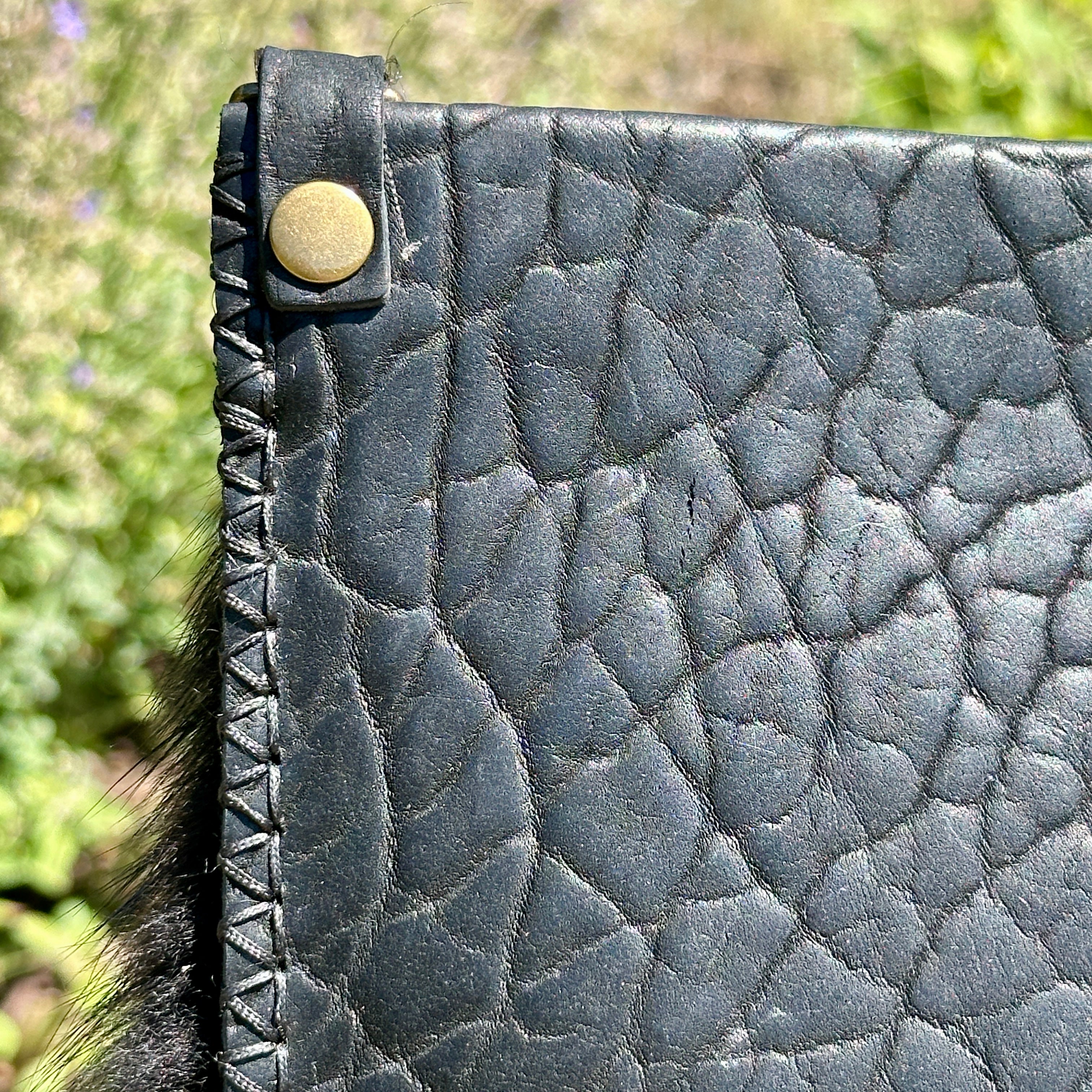 Close-up of the Ana Evening Bag's pebbled black bison leather, hand-stitched edge, and brass rivet