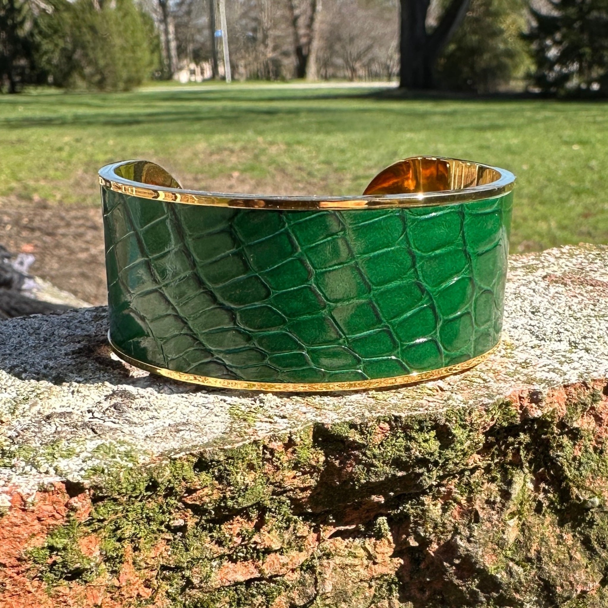 Green crocodile-patterned cuff bracelet with gold accents on a stone surface outdoors.