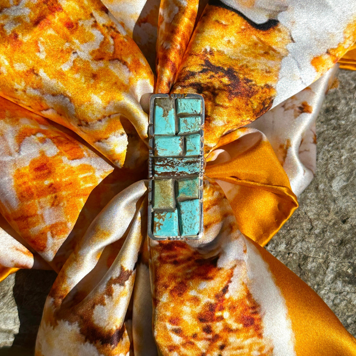 Turquoise cobblestone ring worn as a scarf slide, gathering an orange, gold and cream silk scarf