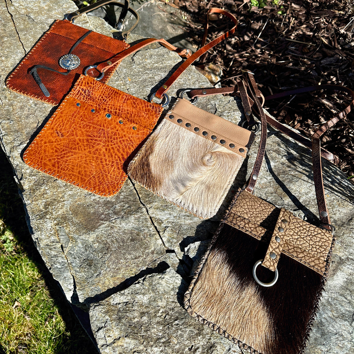 Four Cathay Mini leather crossbody bags in bison, cow and goat hair hide laid out on stone