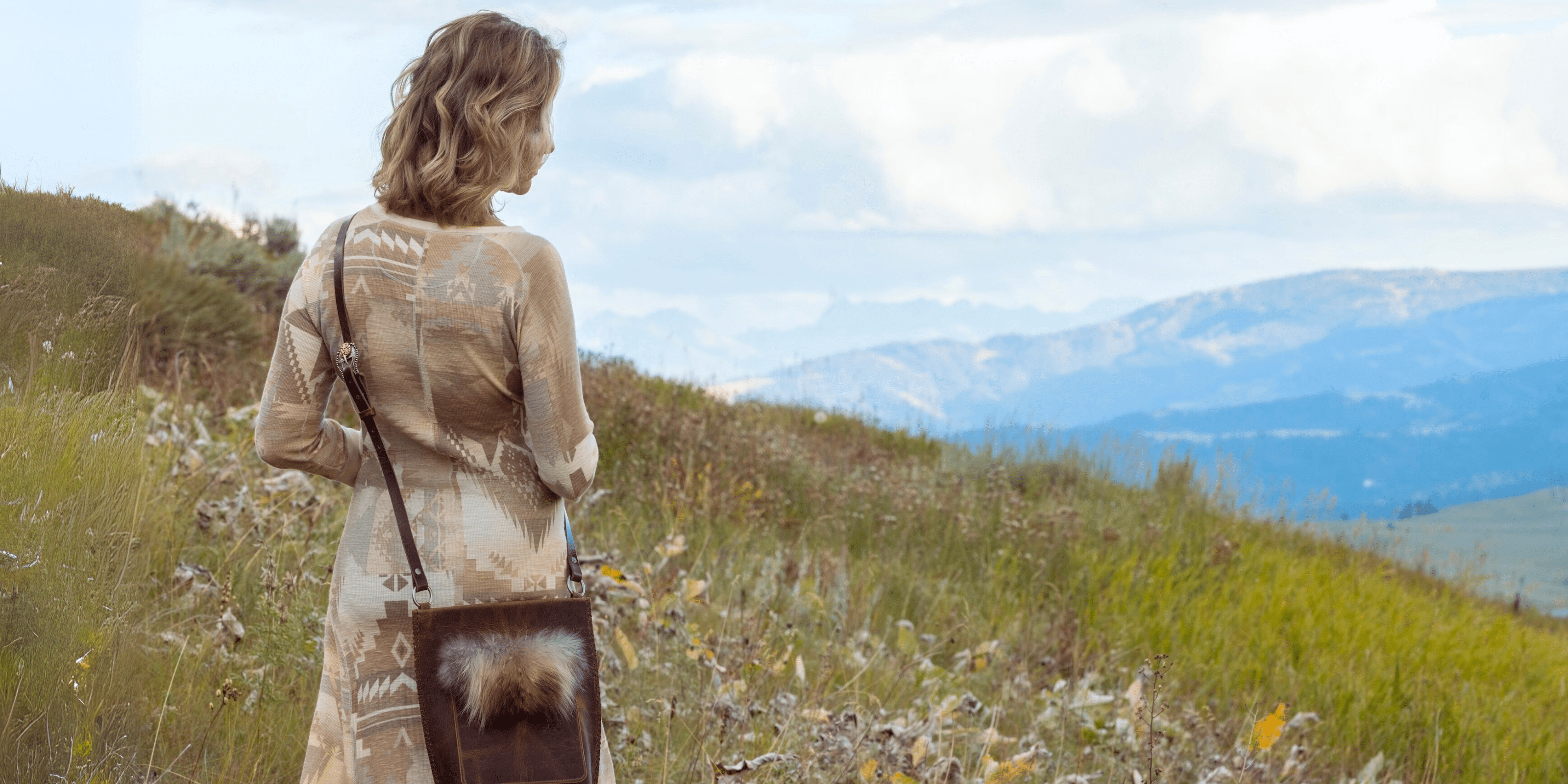 woman standing in a mountain meadow with a leather crossbody bag