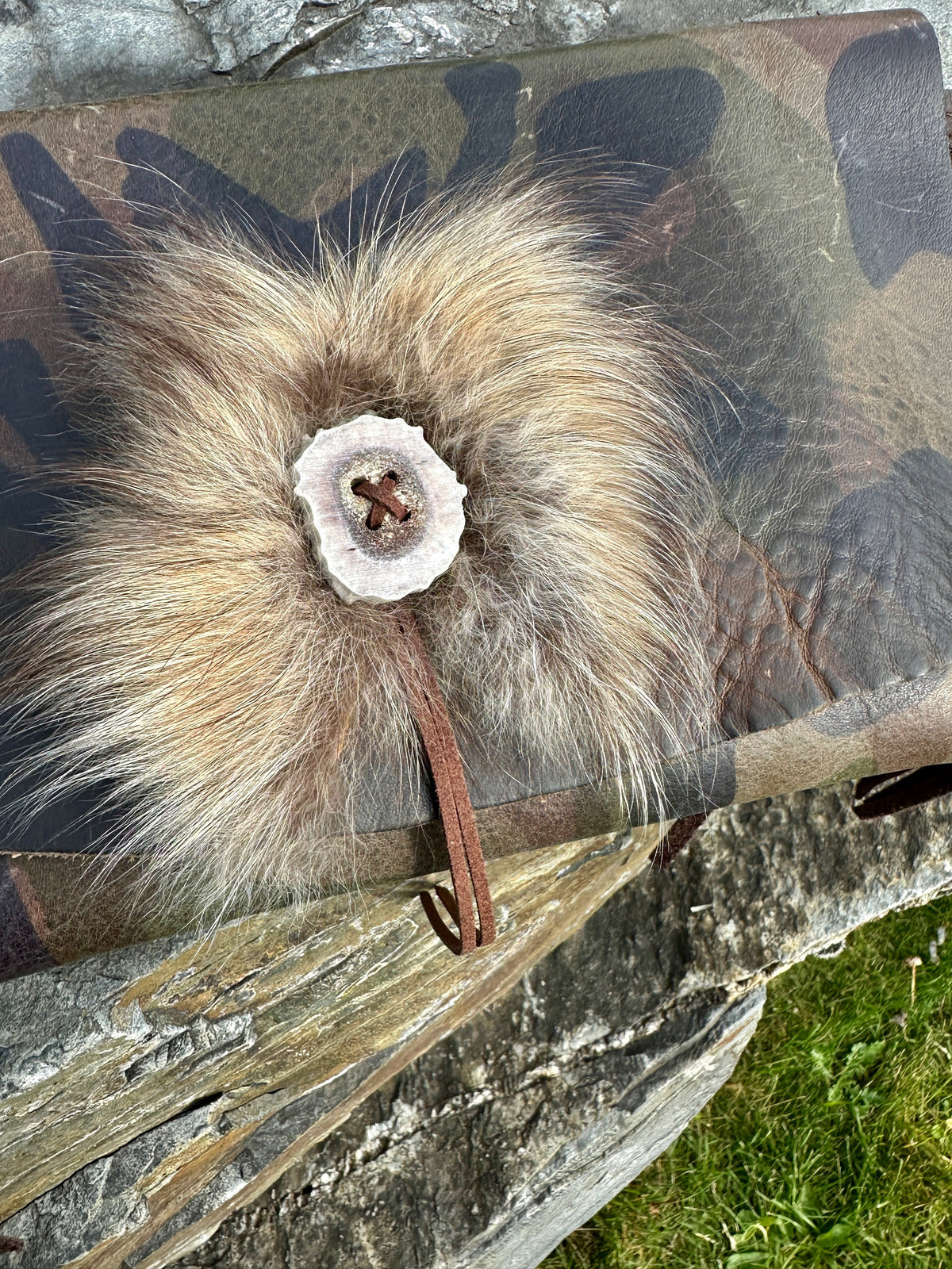 Close-up of the Finn raccoon fur accent and antler button on the Upland Camo Leather Clutch by Bridger Leather, attached with a leather cord to the camo-printed leather flap