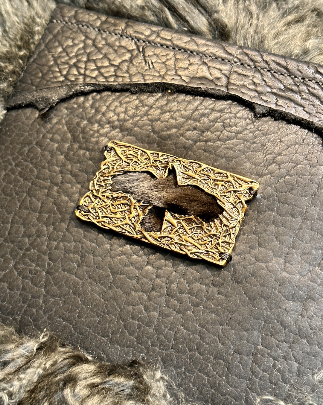 Detail of tote pocket with handmade brass buckle with a raven cut out and fur trim