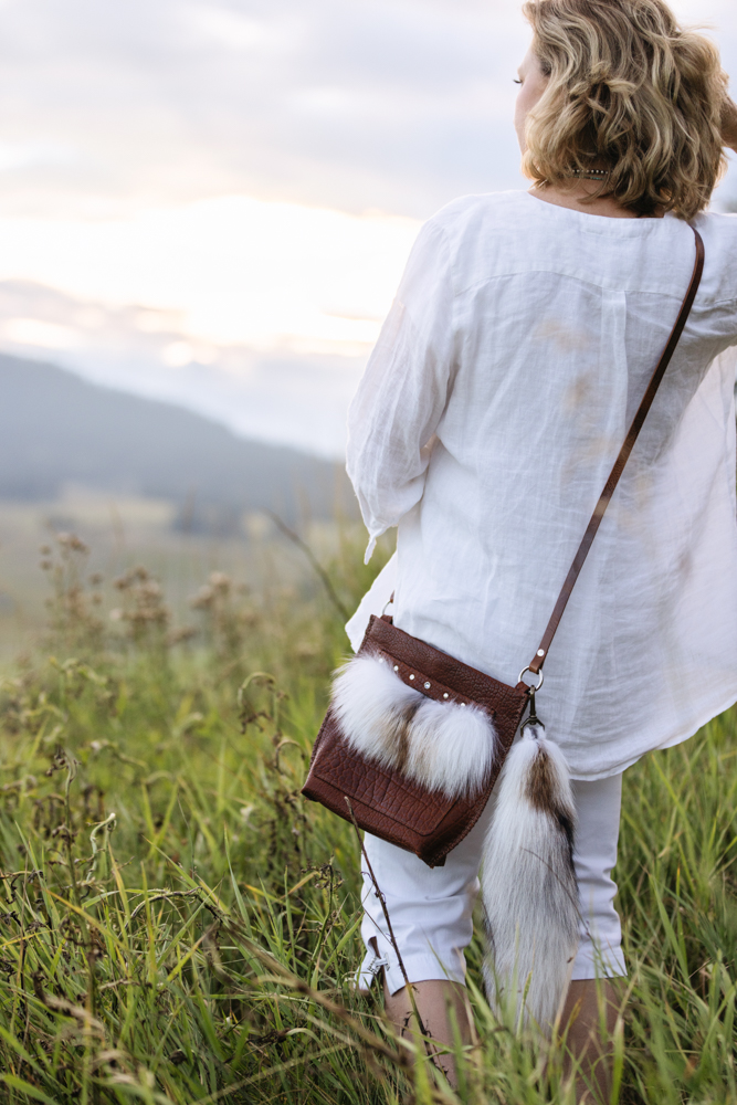 Designer Jenny Keller modeling a bison leather crossbody bag with fox fur trim and fox tail accent.