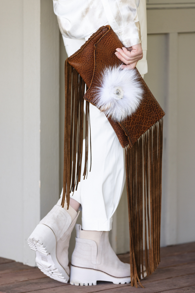 Model posing with a one of a kind bison leather clutch bag trimmed with long fringe and finished with fox fur and elk antler button.
