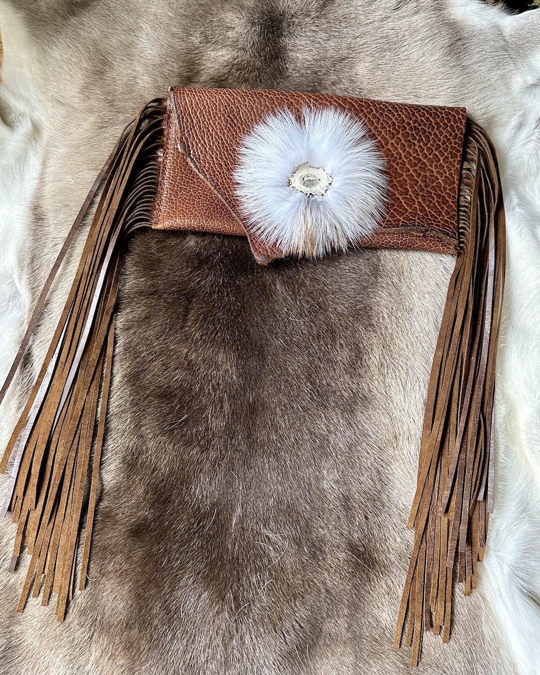One of a kind bison leather clutch bag trimmed with long fringe and finished with fox fur and elk antler button.